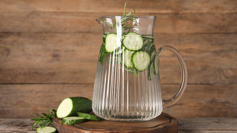 A pitcher of cucumber water on a wooden tray