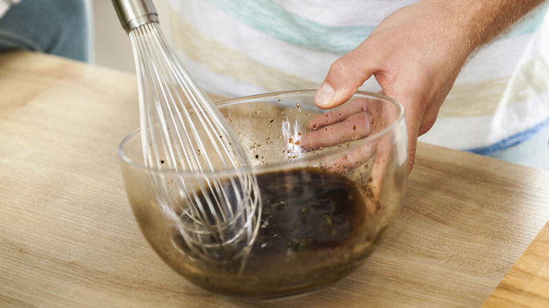 Person whisking soy sauce-based sauce in bowl.