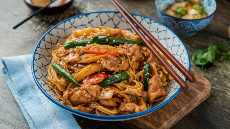 A plate of lo mein, featuring carrots, green onions, and sesame seeds, in a blue bowl with brown chopsticks
