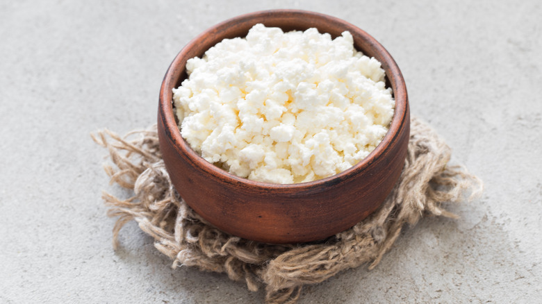A brown wooden bowl filled with cottage cheese, resting on a nest of twine