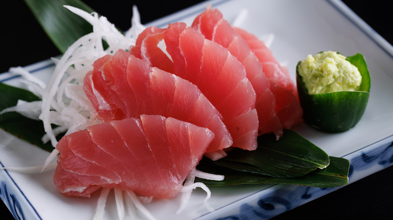 Yellowfin tuna sashimi, with dark pink meat, on a white plate with wasabi