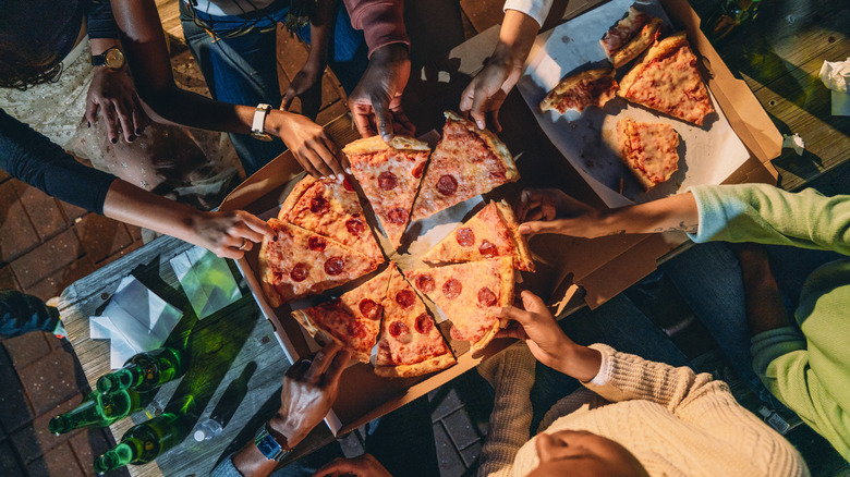 People grabbing pizza slices from box