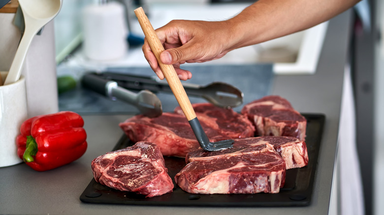 Hands brushing raw steak with marinade on a countertop