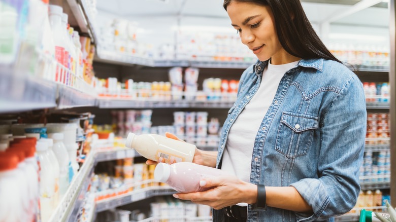 A woman in a store holding two yogurt drinks