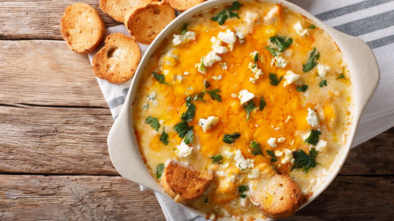 Buffalo chicken dip in crock on wooden table next to crostinis