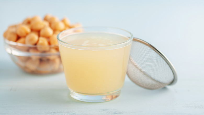 Glass of aquafaba with small bowl of chickpeas