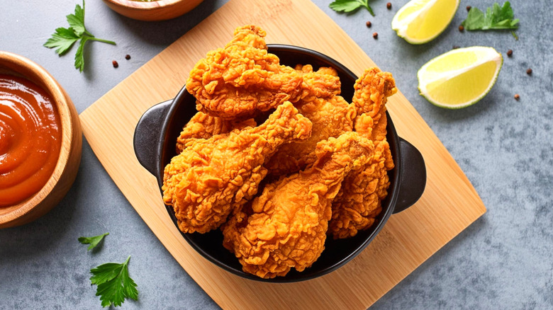 Bowl of fried chicken drumsticks on cutting board