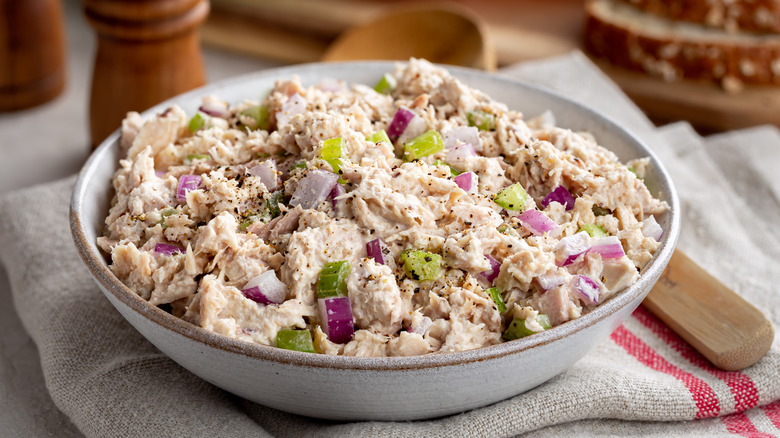Tuna salad in a white bowl on a cloth placemat with a wooden spoon