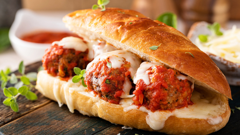 meatball sub sandwich on dark wood cutting board with side of marinara sauce