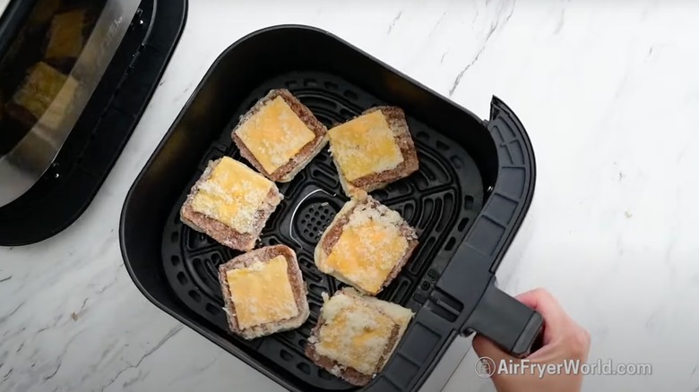 Frozen sliders that have been split in half sitting in an air fryer basket
